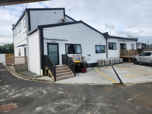 a white house with a car parked in a parking lot at The White House Apartment in Tokoroa