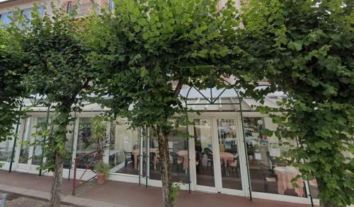 two trees in front of a building with a restaurant at Hôtel des XII Apôtres & de la Clé des Champs in Contrexéville