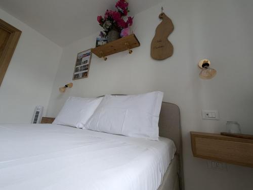 a bed with white sheets and a guitar on the wall at La Casa Della Seta in Mezzegra