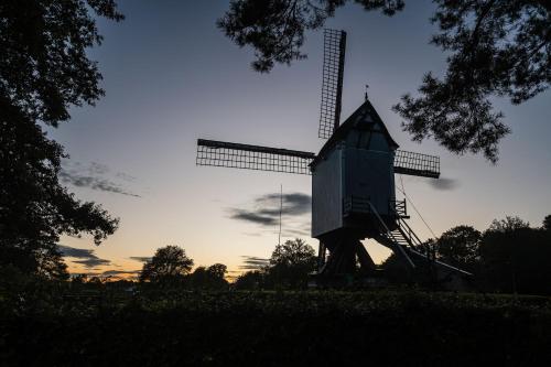 a windmill sitting in a field at sunset at Beddermolen - Molenhuis op historisch erfgoeddomein in Westerlo