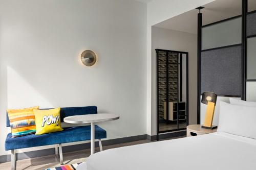 a bedroom with a bed and a blue chair and a table at Aloft Wilmington at Coastline Center in Wilmington