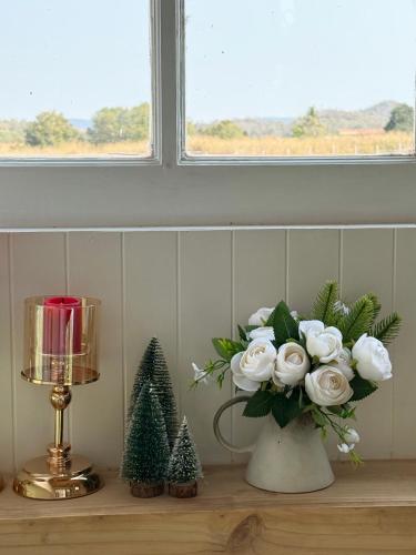 a vase with white roses and christmas trees on a shelf at Tiny Escape Charlotte in Pak Chong