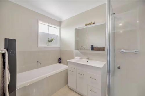 a white bathroom with a tub and a sink and a shower at 4 Bedroom Peaceful stay in Wright with plenty of room to be with family or friends in Weston Creek
