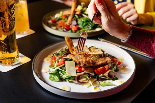 a person eating a salad with a fork on a table at Moxy Milan Linate Airport in Segrate
