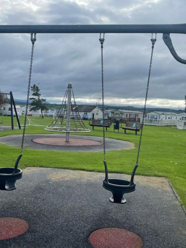 a swing set in a park with a playground at Lyons Manor House Caravan Park in Mawbray