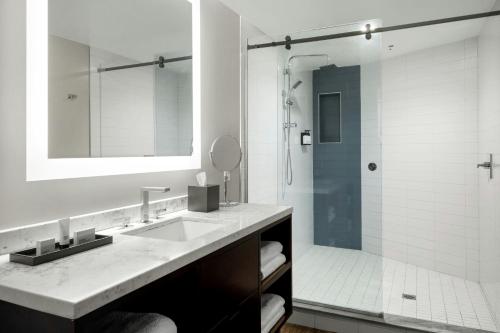 a white bathroom with a sink and a shower at The CURRENT Hotel, Autograph Collection in Tampa