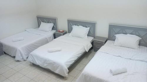 three beds in a room with white sheets and pillows at عمارة المحيسني in Makkah