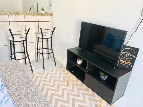 a living room with a tv and two bar stools at Sua Kitnet a menos de 5min da Praia in Santa Cruz Cabrália