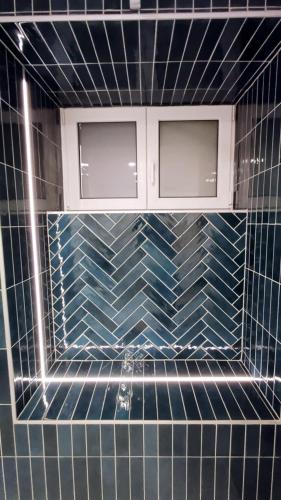 a bathroom with blue tiled walls and two windows at Your Ardennes Adventure - Studio in Jalhay