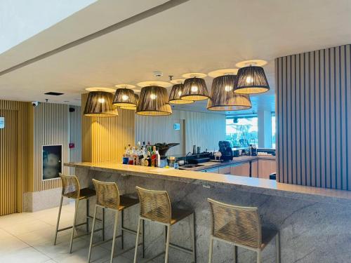 a kitchen with a bar with chairs and lights at Ritz Paradise Beira Mar no Hotel Ritz Suítes in Maceió