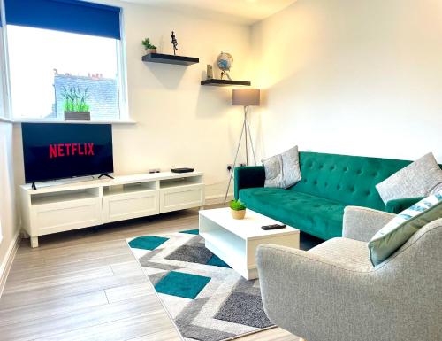 a living room with a green couch and a tv at Central Leigh, on the Broadway, private gated parking, balcony in Southend-on-Sea