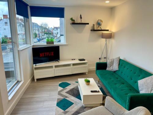 a living room with a green couch and a tv at Central Leigh, on the Broadway, private gated parking, balcony in Southend-on-Sea