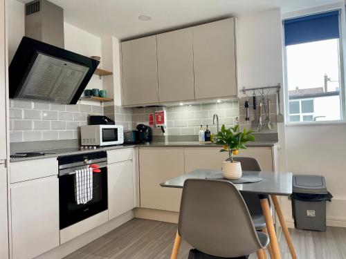 a kitchen with white cabinets and a table with chairs at Central Leigh, on the Broadway, private gated parking, balcony in Southend-on-Sea