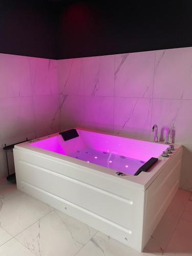 une baignoire blanche avec un éclairage rose dans une salle de bain dans l'établissement Hom & Love, Love Room BDSM, à Homécourt