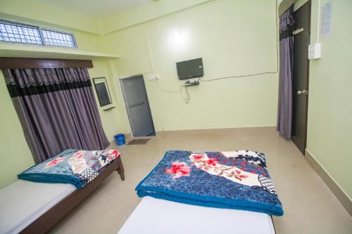a room with two beds and a tv on the wall at Hazarika Lodge and Homestay in Tezpur