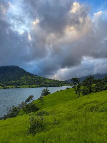 a grassy hill with a lake in the background at Mysticstays Resort in Wai