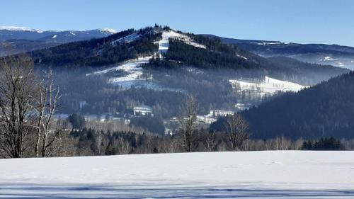 a snow covered hill with a mountain in the background at Chata v Záhoří in Jablonec nad Nisou