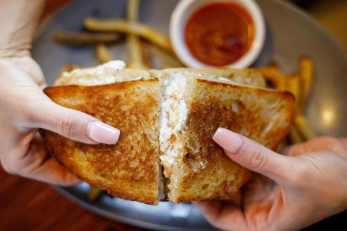 a person holding a grilled cheese sandwich on a plate at Ambassador Hotel Wichita, Autograph Collection in Wichita
