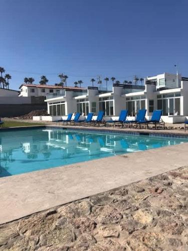 a swimming pool with blue chairs and a building at Beachfront Boutique Villa Cazadores in Rosarito