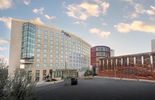 a large building in a parking lot next to two buildings at Signia by Hilton in Amman