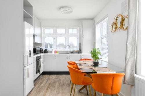 a white kitchen with a table and orange chairs at Modern Flat with Parking, 5 Mins to Tube in Kenton