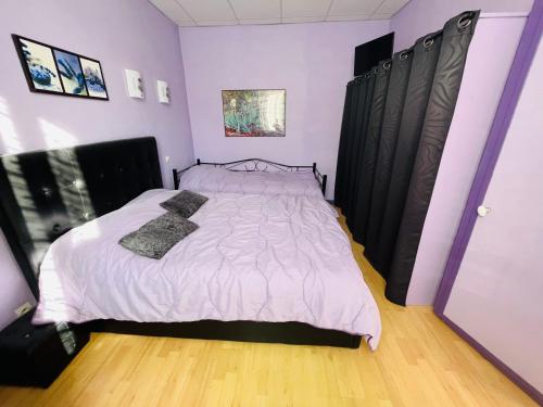 - une chambre dotée d'un lit avec des draps blancs et des murs violets dans l'établissement F2 Pavot, à La Bourboule
