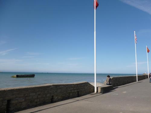 a person sitting on a wall next to the ocean at Studio De La Mer in Arromanches-les-Bains