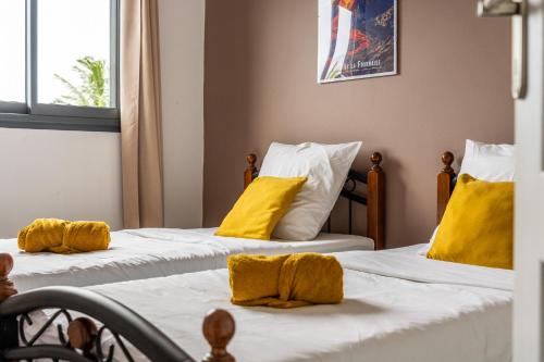 two beds with yellow pillows on them in a room at Évasion Créole à Saint-André II - Parking - Clim in Saint-André