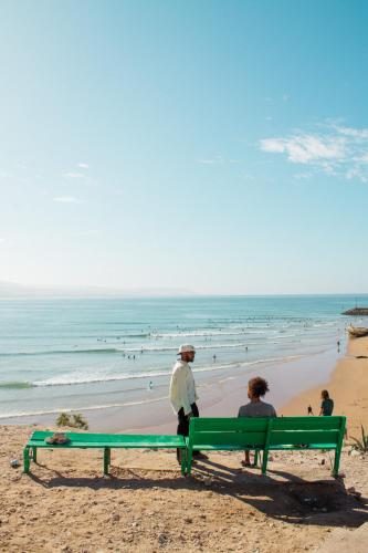 two people sitting on a bench on the beach at Monza Surf House in Tamraght Ouzdar