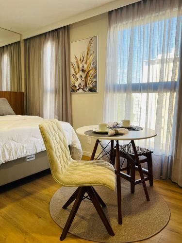 a bedroom with a bed and a table with a chair at LOFT UP 506 | Mobiliado | WIFI | Piscina | Vaga in Blumenau