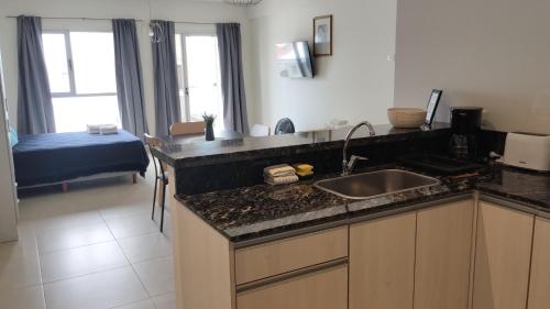a kitchen with a sink and a room with a bed at Leviosa- departamento nuevo con parrilla en el balcón in Puerto Madryn
