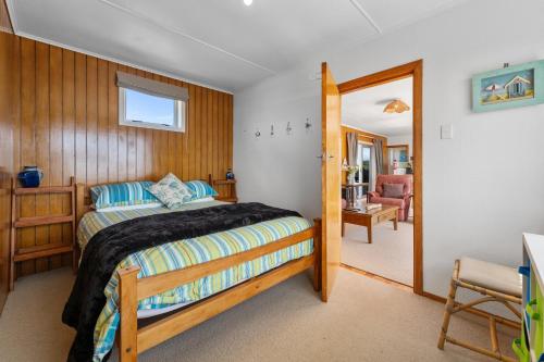 a bedroom with a bed and a chair in it at Kiwi Beach Bach - Waihi Beach Holiday Home in Waihi Beach