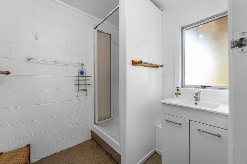 a white bathroom with a sink and a mirror at Kiwi Beach Bach - Waihi Beach Holiday Home in Waihi Beach