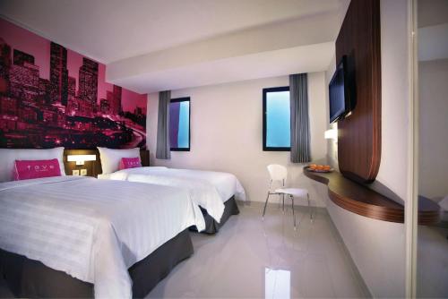 a hotel room with two beds and a flat screen tv at favehotel PGC Cililitan in Jakarta
