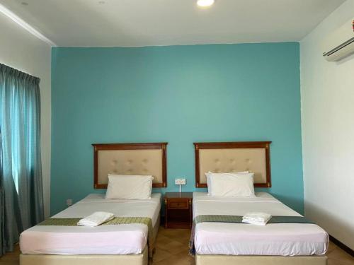 two beds in a room with a blue wall at Capital O 91107 Pd Tiara By Delima Suites in Kampong Batu Empat Belas