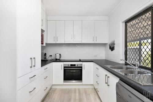 a white kitchen with white cabinets and a sink at Beach vibes in Cooee Bay with high-speed internet in Yeppoon