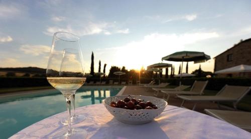 a glass of wine and a bowl of grapes on a table near a pool at Agriturismo La Peschiera in Casole dʼElsa