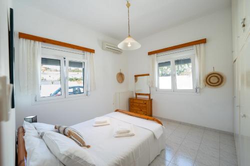 a white bedroom with a bed and two windows at Maria's Home Aegina in Kondós