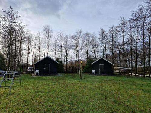 two black buildings in a field with trees at Zilveren maan blokhut 2, trekkershut 2 in De Valom