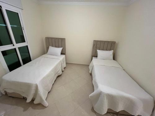 two beds in a small room with a window at 2 Slaapkamer Appartement in Al Azifat