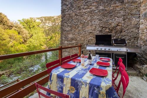d'une table avec des chaises rouges et une cuisinière sur le balcon. dans l'établissement Charmante maison au bord de la rivière, à Saint-Maurice-Navacelles