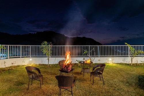 a table and chairs around a fire in a yard at night at ELIVAAS Shourya Sereno - Luxe 4 BHK Villa With Pvt Pool & Garden in Lakāwās