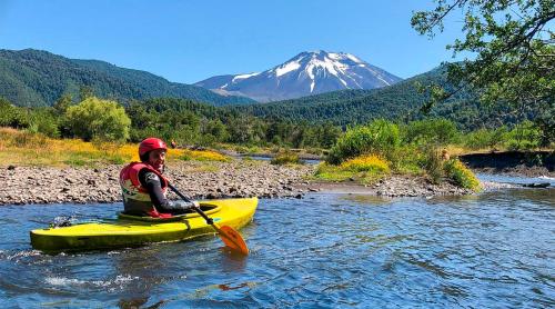 a man in a kayak on a river with a mountain at K10 Lodge in Curacautín
