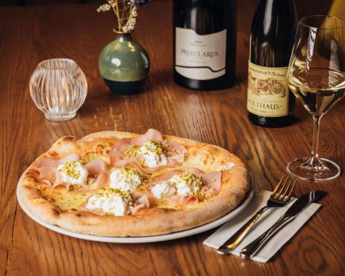 a pizza on a plate on a table with a glass of wine at Aparthotel Maso Corto in Maso Corto