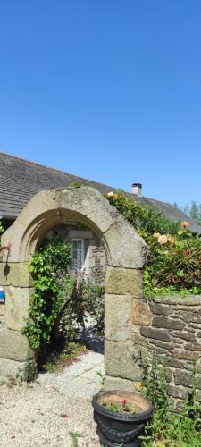 un mur en pierre avec une arche devant une maison dans l'établissement Gîte Les Hortensias Les Jardins de Kerellec 20min de la mer jacuzzi et terrasse, à Plouvorn