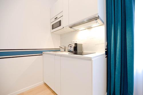 - une cuisine avec des placards blancs et un rideau bleu dans l'établissement CIA - Vosges Gem, à Paris