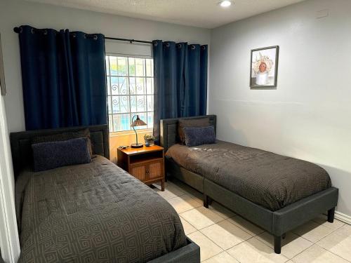 a bedroom with two beds and a window with blue curtains at Tranquil Poolside Oasis with BBQ and Serene Ambiance in North Hollywood