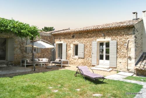 a stone house with a yard with chairs and an umbrella at Villa spacieuse à Oppède avec piscine et vue imprenable in Oppède