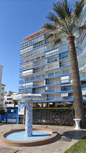 a large building with a palm tree in front of it at Playa y montaña 1ª linea Piscina Parking AC in El Campello