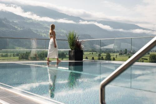 a woman in a white dress walking by a swimming pool at Sportresidenz Zillertal - 4 Sterne Superior in Uderns